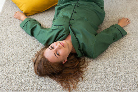 Smiling woman lying on floor in living room in pajama - homewear and free time holidays at home conceptの写真素材
