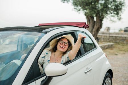 Car driver woman smiling showing new car keys and car. Female driving rented cabrio on summer vacationの写真素材