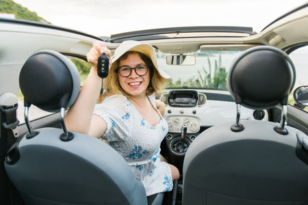 Car driver woman smiling showing new car keys and car. Female driving rented cabrio on summer vacationの写真素材