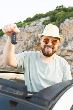 Car driver man smiling showing new car keys and car. Bearded guy driving rented cabrio on summer vacationの写真素材