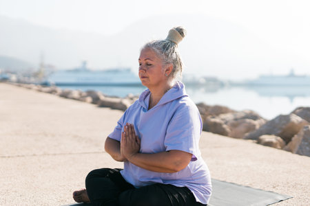 Senior woman with dreadlocks in stretching position by the sea at morning. Elderly woman doing yoga near beach.の写真素材