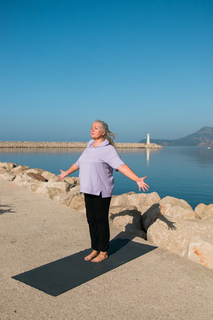 Mature woman with dreadlocks working out doing yoga exercises on sea beach copy space - wellness well-being and active elderly age conceptの写真素材