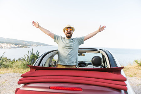 Happy man sitting in white convertible car with beautiful view and having fun - travel summer vacation and rental car conceptの写真素材