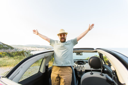 Happy man sitting in white convertible car with beautiful view and having fun - travel summer vacation and rental car conceptの写真素材
