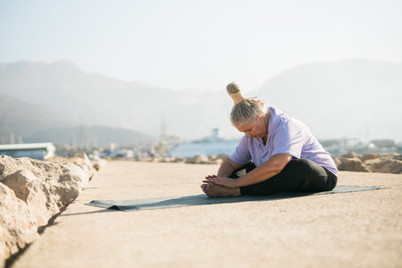 Mature woman with dreadlocks working out doing yoga exercises on sea beach copy space - wellness well-being and active elderly age conceptの写真素材