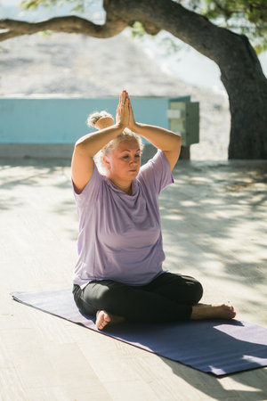 Mature woman with dreadlocks working out doing yoga exercises on sea beach copy space - wellness well-being and active elderly age conceptの写真素材