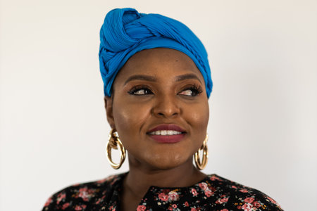 Portrait of cheerful african american woman with headscarf turban against white wall. Happy smiling lady wearing traditional african scarfの写真素材