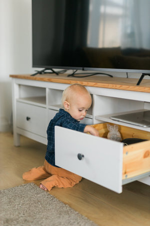 Toddler baby boy open cabinet drawer with his hand. Child explore what is in cabinet. Baby curiosity and child development stagesの写真素材