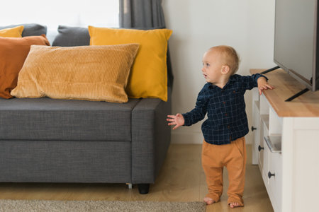 Toddler boy laughing having fun standing near sofa in living room at home copy space. Adorable baby...