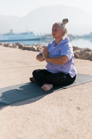 Mindful senior woman with dreadlocks meditating by the sea and beach - wellness and yoga practiceの写真素材