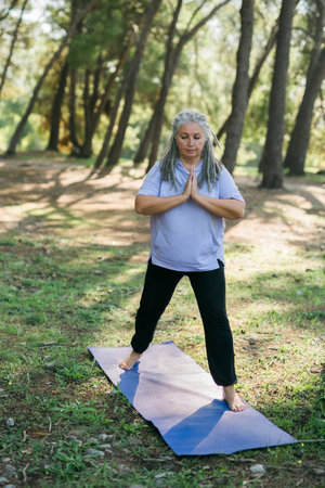 Senior woman with dreadlocks in stretching position on nature at morning. Elderly woman doing yoga on park - wellbeing and wellness tai chiの写真素材