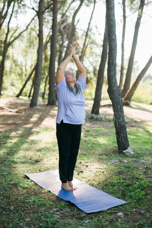 Senior woman with dreadlocks in stretching position on nature at morning. Elderly woman doing yoga on park - wellbeing and wellness tai chiの写真素材