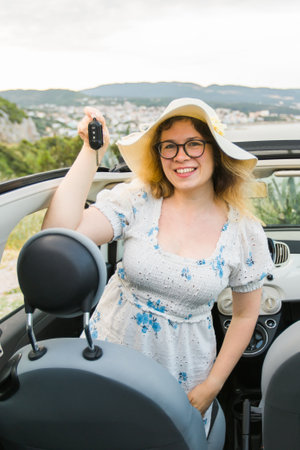 Car driver woman smiling showing new car keys and car. Female driving rented cabrio on summer vacationの写真素材