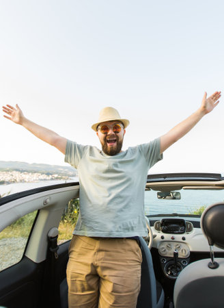 Happy man sitting in white convertible car with beautiful view and having fun - travel summer vacation and rental car conceptの写真素材