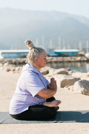 Mature elderly woman with dreadlocks doing pose during yoga training in park on summer day, healthy active senior female practicing asana on mat in morning on fresh airの写真素材