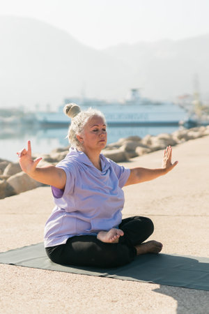 Serious aged woman in with dreadlocks hairstyle standing on beach against sea while practicing pose or asana during sunny dayの写真素材