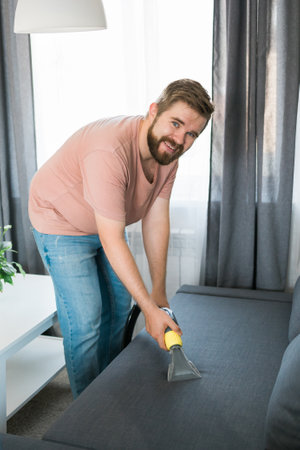 Man holding modern washing vacuum cleaner and cleaning dirty sofa with professionally detergent. Professional springclean at home conceptの写真素材
