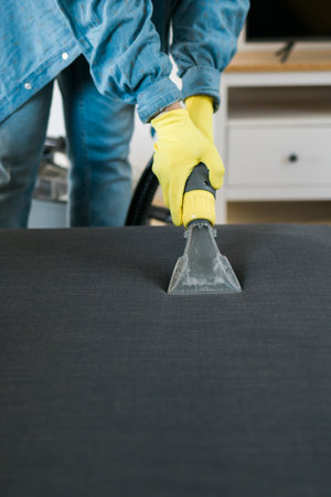 Cleaning service company employee removing dirt from furniture in flat with professional equipment....