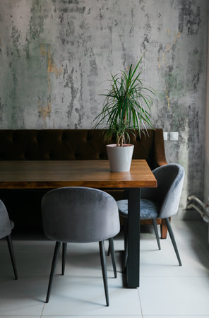 Grey chairs at wooden table and green plant in pot in minimalist cafe interior with windowの写真素材