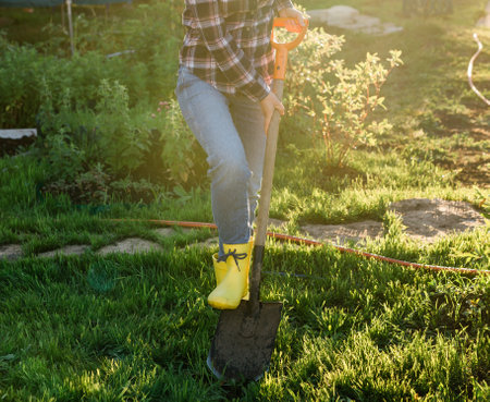 Positive female gardener digs the beds with shovel on sunny warm spring day. Plant care and planting...