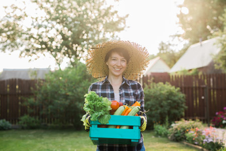 Female farmer carrying box of picked vegetables - garden and harvesting agricultural product for online selling.の写真素材