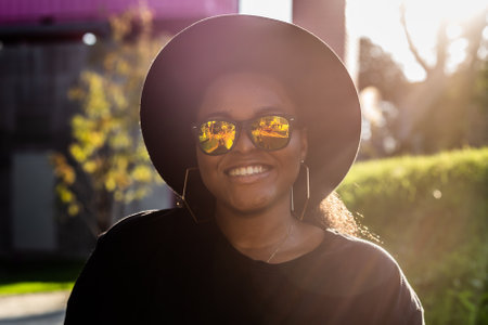 Happy African american young woman wearing t-shirt laughing looking at camera standing on street. Smiling generation z hipster girl posing outdoor backlit with sunlight portraitの写真素材
