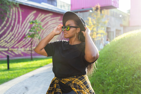 Happy African american young woman wearing t-shirt laughing looking at camera standing on street. Smiling generation z hipster girl posing outdoor backlit with sunlight portraitの写真素材