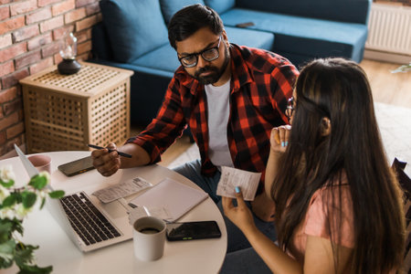 Serious wife and husband planning budget, checking finances, focused young woman using online calculator and counting bills or taxes, man using laptop, online banking services. Family sitting at table in kitchen - economic crisis conceptの写真素材