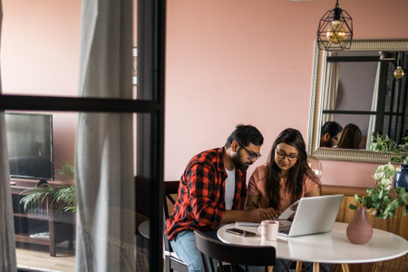 Young millennial indian husband and wife doing domestic paperwork, accounting job and reviewing paper bills, receipts at laptop computer, using online calculator and paying mortgage rent fees on internet - economic crisis conceptの写真素材