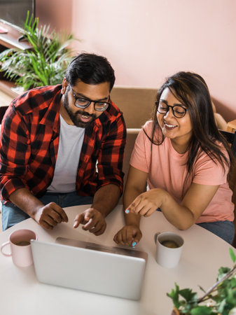 Latino or indian man and woman couple use their laptop in the living room to make video calls. Video call and online chat with familyの写真素材