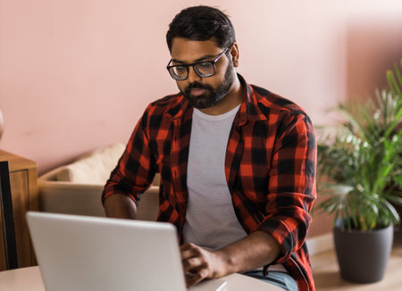 technology remote job and lifestyle concept - happy indian man in glasses with laptop computer working at home officeの写真素材
