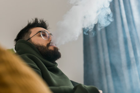 Bearded man is smoking hookah at home and blowing cloud of smoke - chill time and resting conceptの写真素材