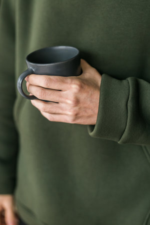 Close-up man with cup of coffee. Guy drinks coffee sitting near windowの写真素材