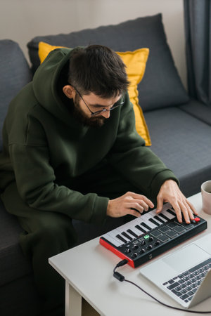 Man recording electronic music track with portable midi keyboard on laptop computer in home studio. Producing and mixing music beat making and arranging audio content with professional audio devicesの写真素材
