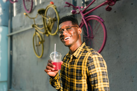 Young cheerful african american male on city having fun and holding cocktail. Man on summer holiday. Leisure lifestyle holiday and summer drinks conceptの写真素材