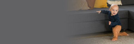 Banner Toddler boy laughing having fun standing near sofa in living room at home copy space....