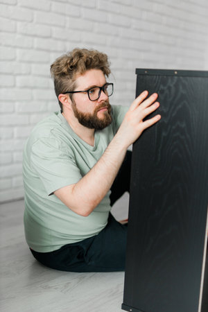 Bearded attractive man assembles furniture - handwerker and interior objects conceptの写真素材