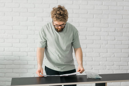 Bearded millennial man assemble his bookcase. He uses tools for furniture. Furniture for the...