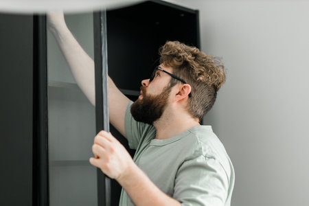 Bearded millennial man assemble his bookcase. He uses tools for furniture. Furniture for the interior room or apartmentsの写真素材