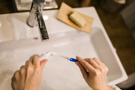 Female hand holding toothbrush with toothpaste applied on it in bathroom. Close up of female hand ready for brushing teeth. Young woman hand holding toothbrush with white tooth paste.の写真素材