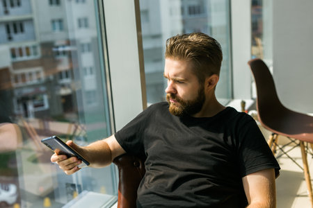 Fashionable young bearded guy wears stylish clothes and trendy hairstyle and happy to exchange messages with friends and uses free internet connection on electronic modern gadget copy space - social networks and life online conceptの写真素材