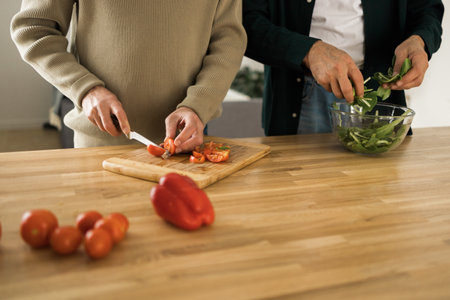 Two unrecognizable senior men cutting tomatoes on a chopping board at kitchenの写真素材