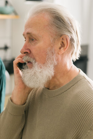 Happy bearded aged senior man talking by phone at home - active senior aged and communication conceptの写真素材
