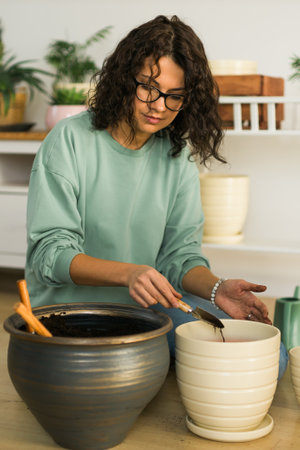 Smiling young woman and pot with plant happy work in indoor garden or cozy home office with different houseplants. Happy millennial female gardener or florist take care of domestic flowerの写真素材