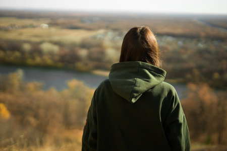 Rear view of trendy young woman in dark green hoodie in autumn copy space. Cute model walks in park in golden autumn through colorful trees and fallen leaves. Autumn fall walk colorful natureの写真素材
