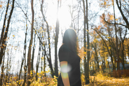 Cute young woman with long fluffy hair dancing in a park at sunset. Beautiful young woman with brown...
