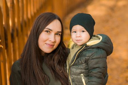 Cute little asian boy stands with mother outdoors. Happy child walking in autumn park. Toddler baby...