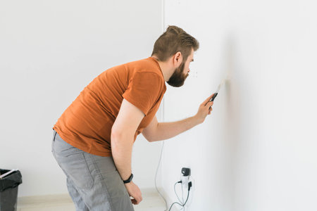 Young man using spatula and plastering of wall with white fresh finishing putty. Closeup. Repair work of home. Side view.の写真素材