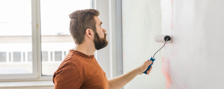 Banner man painting wall with paint roller - renovation and redecoration conceptの写真素材