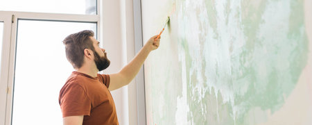 Man smoothes wall surface with a wall grinder banner copy space. Male grind a white plaster wall - renovation and redecoration concept. Copy space and empty space for textの写真素材